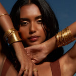 A woman showcasing the Gold Large Bangle Bracelet Cuff - Something Special amidst a backdrop of blue skies, embodying the essence of spiritual jewelry and protection with its elegant design, perfect for meditation gifts and meaningful expressions of yoga and manifestation.