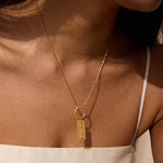 Gold-toned necklace with rectangular charm engraved with "222" worn close to chest.