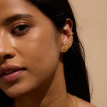 Gold-toned wing-shaped stud earrings worn on woman's earlobe against neutral background.