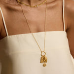 Gold-toned pendant necklace with rectangular charm, fan detail, and small circular charm hanging from delicate chain.