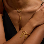 Gold necklace with angel wing pendant and matching bracelet with wing charm worn on model's neck and wrist.