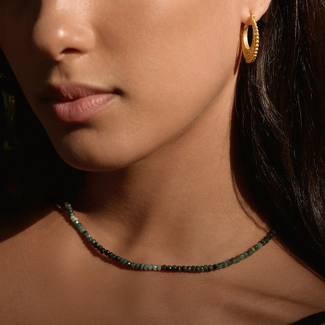 A close-up of a woman wearing the Shades of Wisdom 14kt Gold Emerald Necklace, featuring varying shades of emerald gemstones that symbolize wisdom and abundance. This spiritual jewelry piece serves as a meaningful talisman for meditation and protection, connecting with the energies of the sun and moon, perfect for yoga and manifestation practices.