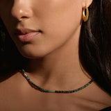 A close-up of a woman wearing the Shades of Wisdom 14kt Gold Emerald Necklace, featuring varying shades of emerald gemstones that symbolize wisdom and abundance. This spiritual jewelry piece serves as a meaningful talisman for meditation and protection, connecting with the energies of the sun and moon, perfect for yoga and manifestation practices.