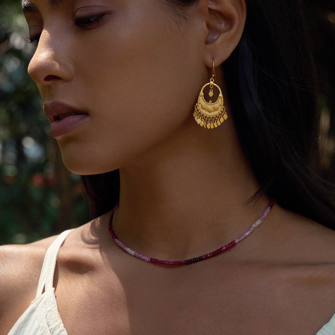 Close-up of a model wearing the Shades of Passion 14kt Gold Ruby Necklace alongside golden earrings, embodying the spirit of spiritual and meaningful adornment suitable for manifestation and zodiac energy.