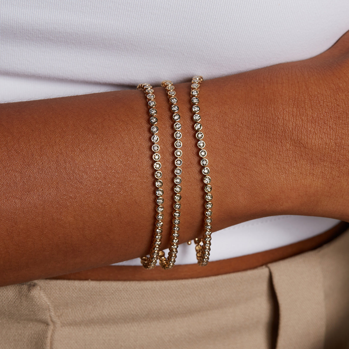 A close-up of a person's wrist adorned with three elegant Diamond 14kt Gold Tennis Bracelets, showcasing spiritual jewelry that enhances meditation and brings abundance. These bracelets serve as meaningful talismans for protection, ideal for yoga enthusiasts.