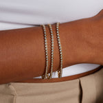 A close-up of a person's wrist adorned with three elegant Diamond 14kt Gold Tennis Bracelets, showcasing spiritual jewelry that enhances meditation and brings abundance. These bracelets serve as meaningful talismans for protection, ideal for yoga enthusiasts.
