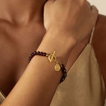 A close-up of the Balanced Beginnings Garnet Lotus Bracelet showcased on a model's wrist, highlighting the grounding garnet stones and lotus charm, ideal for yoga enthusiasts and those interested in talismans for spiritual protection.