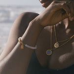 A serene beach setting highlights the Divine Knowing Moonstone Bracelet on a model's wrist, accentuating its moonstone beauty. Represents spiritual jewelry, meditation, and serves as a powerful talisman for protection and meaningful manifestation aligned with the sun and moon.