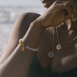 A serene beach setting highlights the Divine Knowing Moonstone Bracelet on a model's wrist, accentuating its moonstone beauty. Represents spiritual jewelry, meditation, and serves as a powerful talisman for protection and meaningful manifestation aligned with the sun and moon.