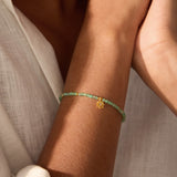 Close-up of the Emerald Lotus May Birthstone Bracelet worn on a wrist, displaying its stunning emerald stones and gold details, ideal for enhancing your spiritual journey, meditation, and connection to the zodiac while serving as a meaningful talisman of abundance and transformation.