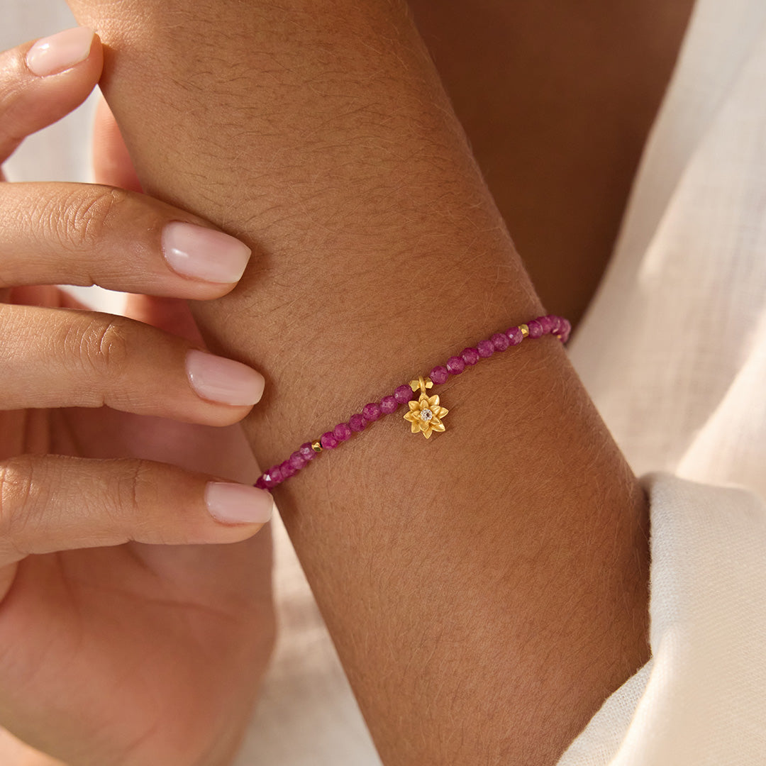 Ruby Lotus July Birthstone Bracelet worn elegantly on a wrist, showcasing its vibrant ruby beads and gold lotus pendant. This spiritual jewelry piece embodies meaning and serves as a talisman for mindfulness, protection, and zodiac energy in daily life.