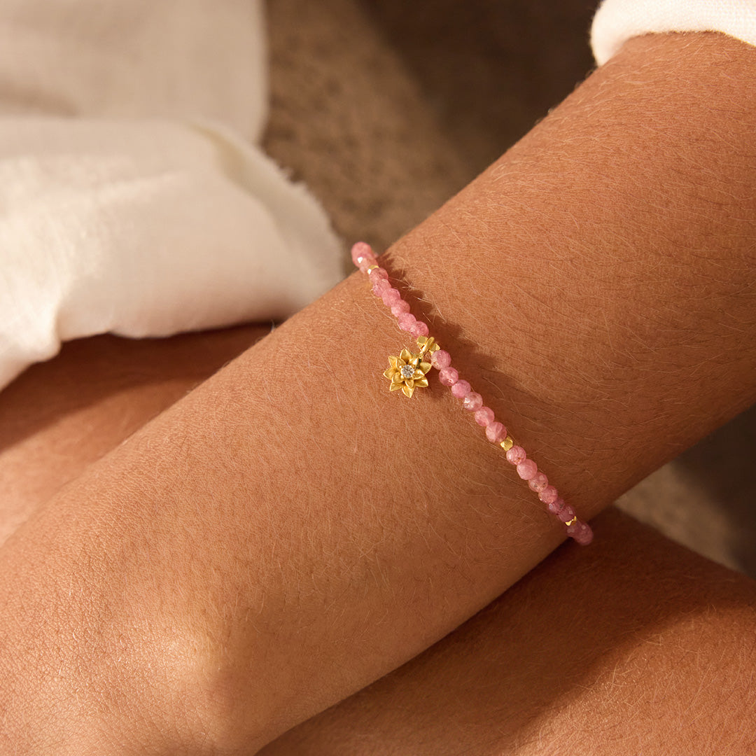 A close-up image of the Pink Tourmaline Lotus October Birthstone Bracelet, featuring a delicate lotus flower pendant in 18kt gold, surrounded by pink tourmaline beads. This spiritual jewelry represents meditation and serves as a talisman for those seeking spiritual alignment, meaning and manifestation in their lives. A beautiful accessory for yoga practitioners and zodiac enthusiasts, celebrating the sun and moon's energy while enhancing personal protection and creativity.