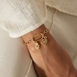 Gold-tone chain bracelet with lotus and evil eye charm pendants worn on wrist.