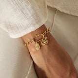 Gold-tone chain bracelet with lotus and evil eye charm pendants worn on wrist.