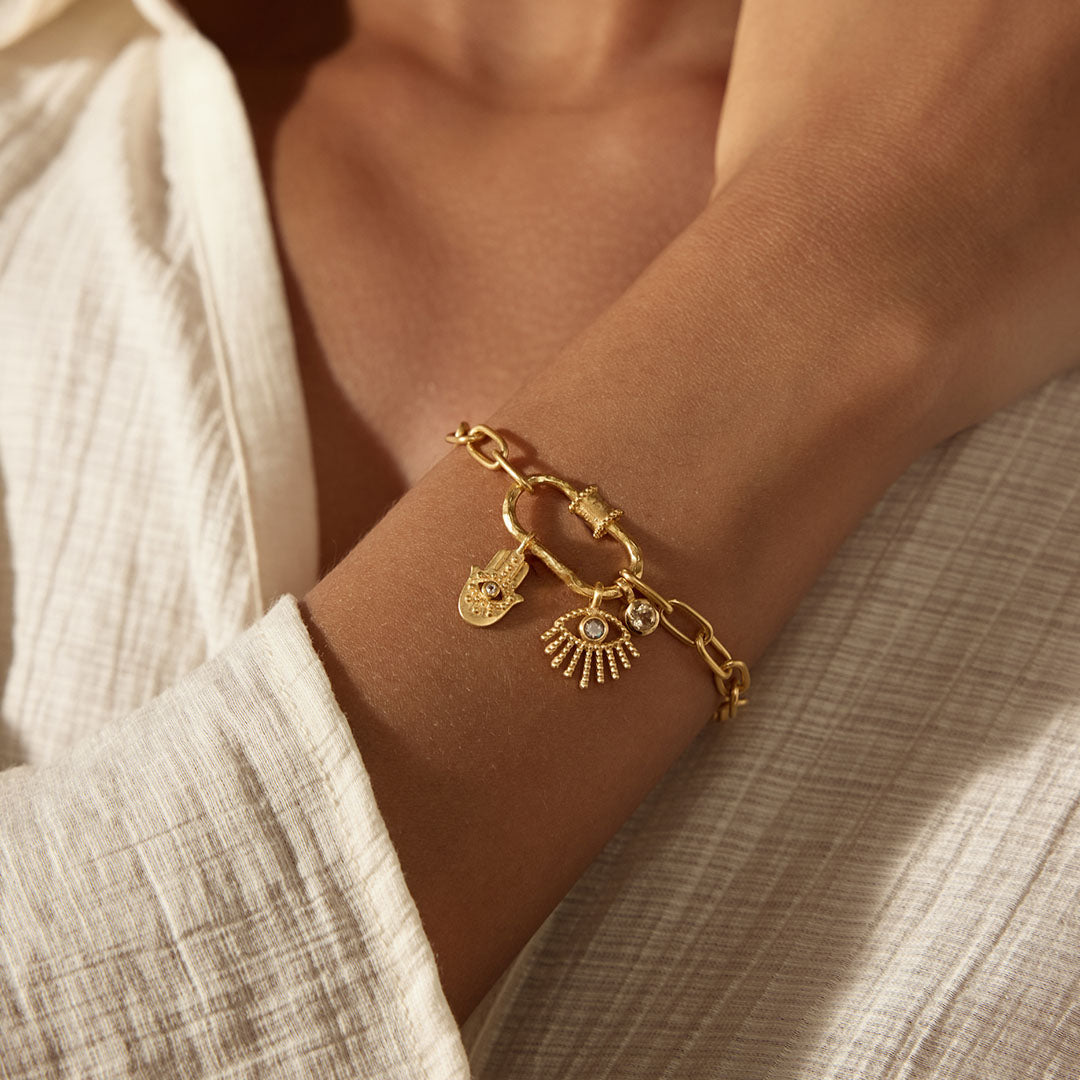Gold-toned chain bracelet with decorative charms including a lotus flower and shell pendant worn on wrist.
