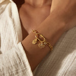 Gold-toned chain bracelet with decorative charms including a lotus flower and shell pendant worn on wrist.