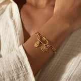 Gold-toned chain bracelet with decorative charms including a lotus flower and shell pendant worn on wrist.