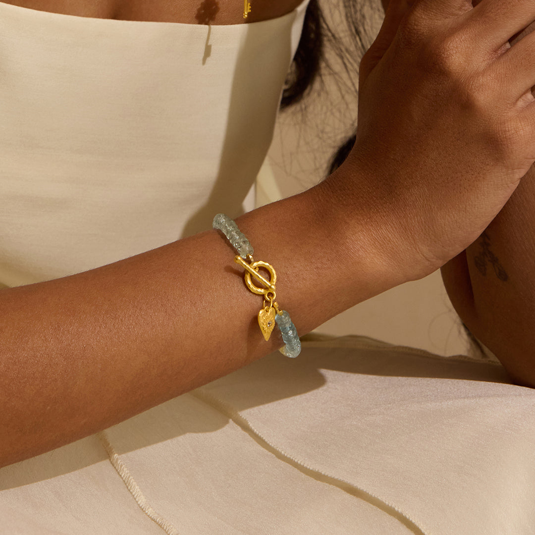 The Tranquil Spirit Aquamarine Heart Toggle Bracelet on a wrist, showcasing its radiant aquamarine and gold elements. This spiritual jewelry piece is ideal for meditation and serves as a meaningful talisman for zodiac enthusiasts, promoting protection and peace while enhancing yoga practices under the sun and moon.