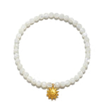 Stretch bracelet with white mother of pearl beads and gold-tone sun charm pendant.