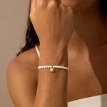 White mother of pearl beaded stretch bracelet with small gold sun charm worn on wrist.