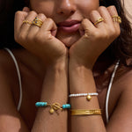 Stretch bracelet with white mother-of-pearl beads, gold-tone sun charm, and adjustable fit worn on wrist.