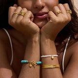 Stretch bracelet with white mother-of-pearl beads, gold-tone sun charm, and adjustable fit worn on wrist.