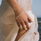 Two-strand bracelet with white pearl beads and gold chain worn on wrist with matching gold ring.