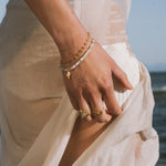 Gold chain bracelet with white beads and small gold charm pendant worn on wrist.