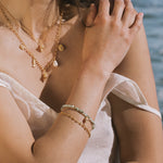 Gold chain bracelet with green beaded section and small gold charm detail worn on wrist.