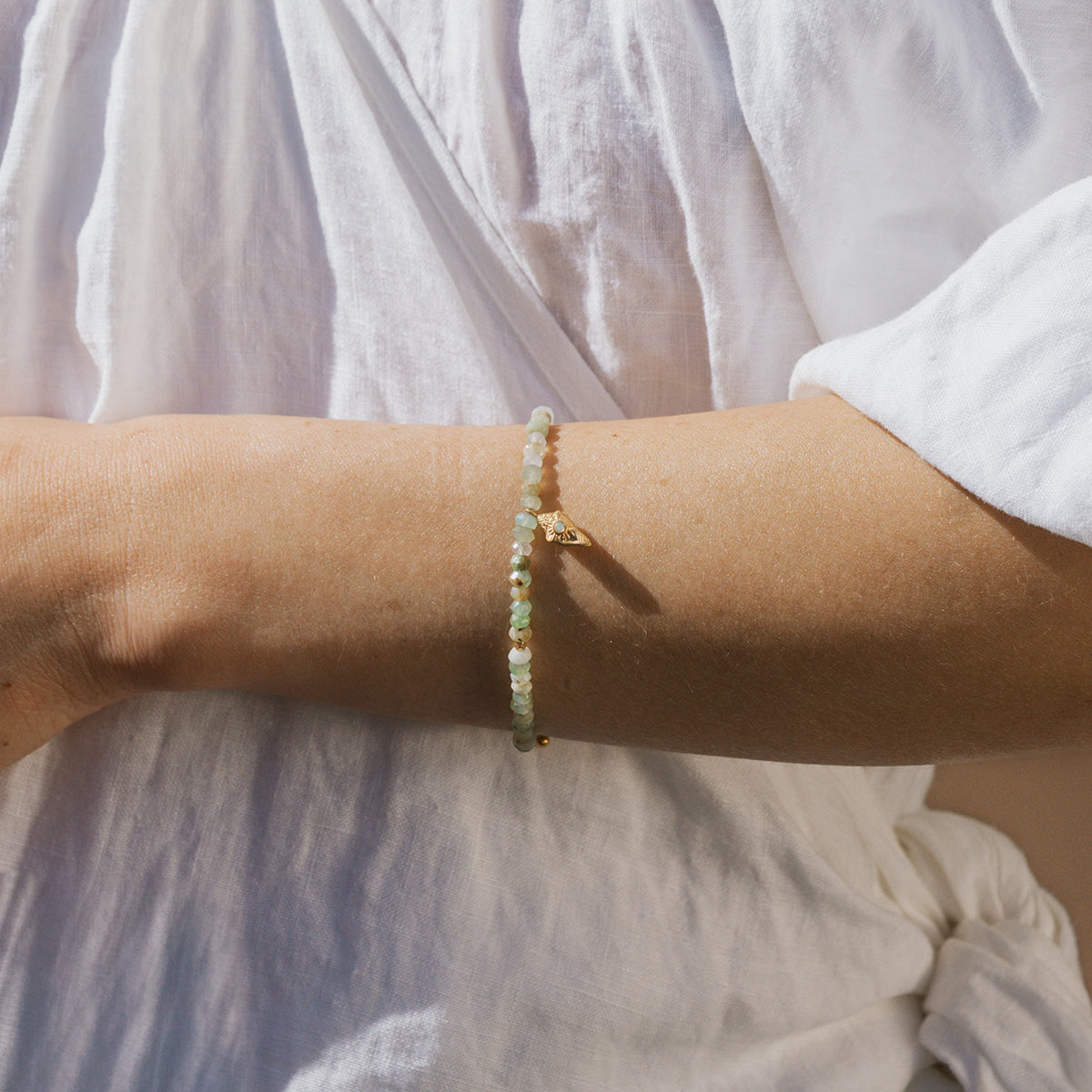 Beaded bracelet with pale green and white stones strung together, worn on wrist over white fabric.