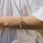 Beaded bracelet with pale green and white stones strung together, worn on wrist over white fabric.