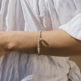 Beaded bracelet with pale green and white stones strung together, worn on wrist over white fabric.