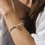 Beaded bracelet with pale green and cream stones and gold-tone charm worn on wrist.
