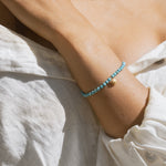 Turquoise beaded stretch bracelet worn on wrist with small gold charm detail.