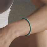 Turquoise beaded stretch bracelet worn on wrist with small round beads throughout.