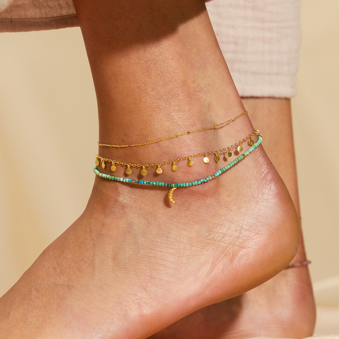 Elegant view of the Moonlit Journey Turquoise Moon Anklet layered with delicate gold chains, showcasing its beautiful turquoise beads and moon charm. This spiritual jewelry is designed for those seeking protection and inspiration during their journey in meditation and yoga, serving as a meaningful charm for manifestation.