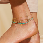 Stylishly layered anklets featuring the Walk with Joy Coin Chain Anklet, showcasing a fusion of colors and textures. This spiritual jewelry piece resonates with the energies of the sun and moon, ideal for yoga enthusiasts and those seeking meaningful adornments for their spiritual journey.