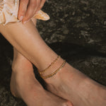 Gold-toned ankle bracelets with beaded and chain link designs worn on person's ankle.