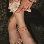 Gold-toned anklet with small beaded or spherical details worn on ankle.