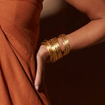 Close-up of the Gold Large Bangle Bracelet Cuff - Something Special worn by a woman in a warm-toned outfit, reflecting the beauty of symbolic adornments in spiritual jewelry, ideal for mantra chanting and adding a touch of zodiac charm.