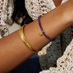 An elegant view of the Tranquility Lotus Amethyst Gemstone Bracelet alongside other gold bangles, highlighting its significance as spiritual jewelry, ideal for meaningful expressions of manifestation, connected to zodiac energies, perfect as an amulet for meditation and yoga.