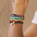 The Heart Chakra Aventurine Stretch Bracelet displayed on a wrist adorned with multiple spiritual jewelry pieces, symbolizing protection and meaningful meditation practices. This vibrant collection represents connection to the sun, moon, and zodiac, enhancing manifestation during yoga and daily activities.
