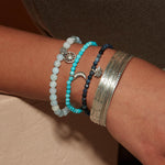 A wrist adorned with the Small Silver Multi Bangle Cuff alongside various beads, reflecting a blend of styles that resonates with spiritual jewelry themes. These pieces serve as meaningful reminders for meditation and yoga, offering manifestation and protection.