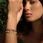 Multiple beaded bracelets with purple amethyst and multicolored stones worn on wrist with gold-tone charms.