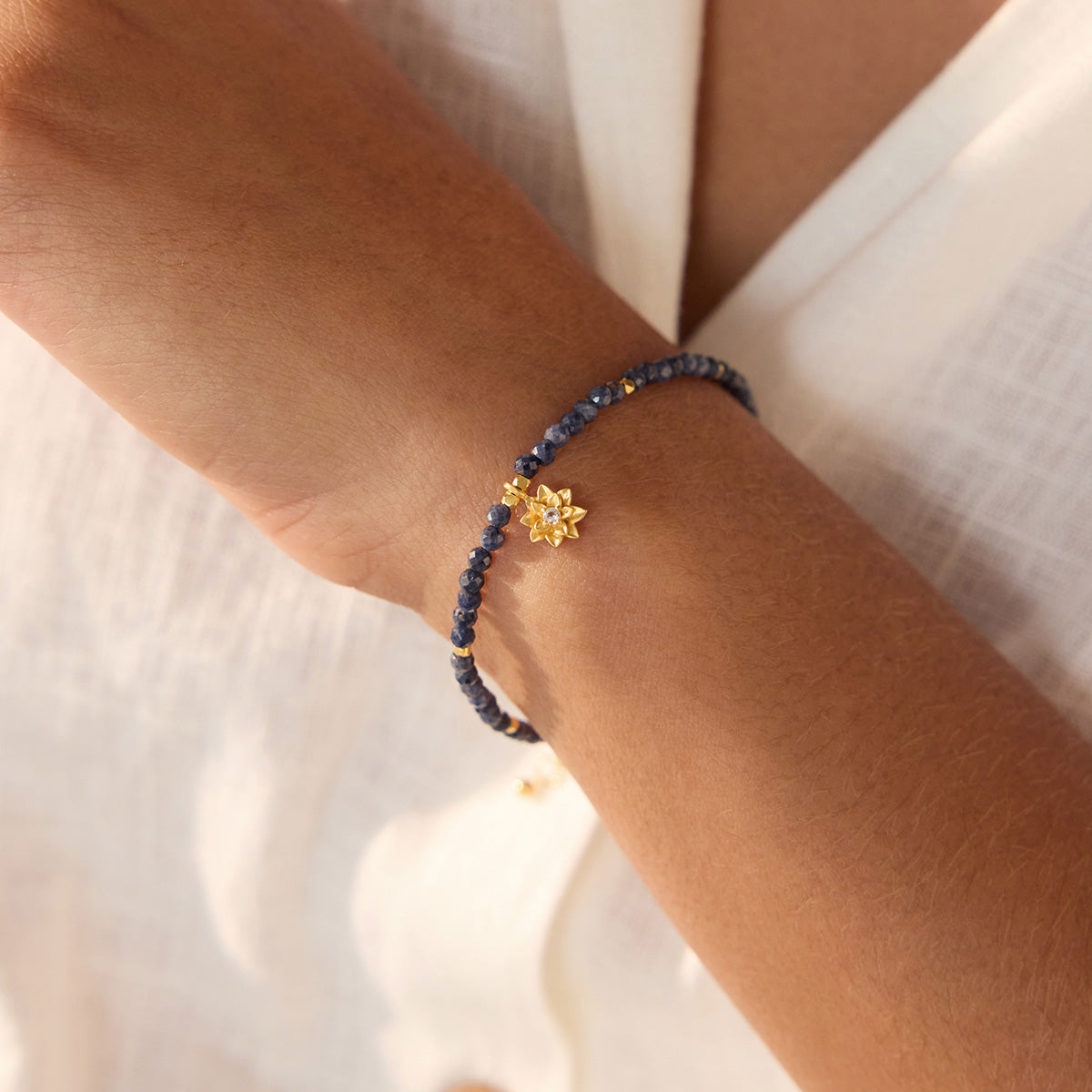 Beaded bracelet with dark blue sapphire stones and gold-tone lotus flower charm worn on wrist.