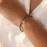 Beaded bracelet with dark blue sapphire stones and gold-tone lotus flower charm worn on wrist.