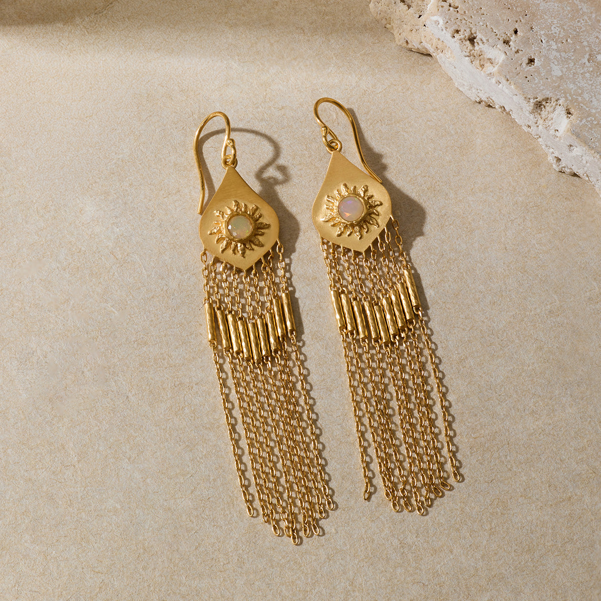 Pair of gold-toned drop earrings with sun motif tops and long chain fringe, displayed on neutral surface.