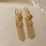 Pair of gold-toned drop earrings with sun motif tops and long chain fringe, displayed on neutral surface.