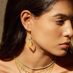 Side view of a woman adorned with Transformed by Compassion Lotus Blue Topaz Earrings, showcasing their unique lotus petal design. Crafted in 18kt gold plating, these earrings embody the essence of spiritual jewelry, perfect for those seeking charm and inspiration in their yoga and meditation practices.