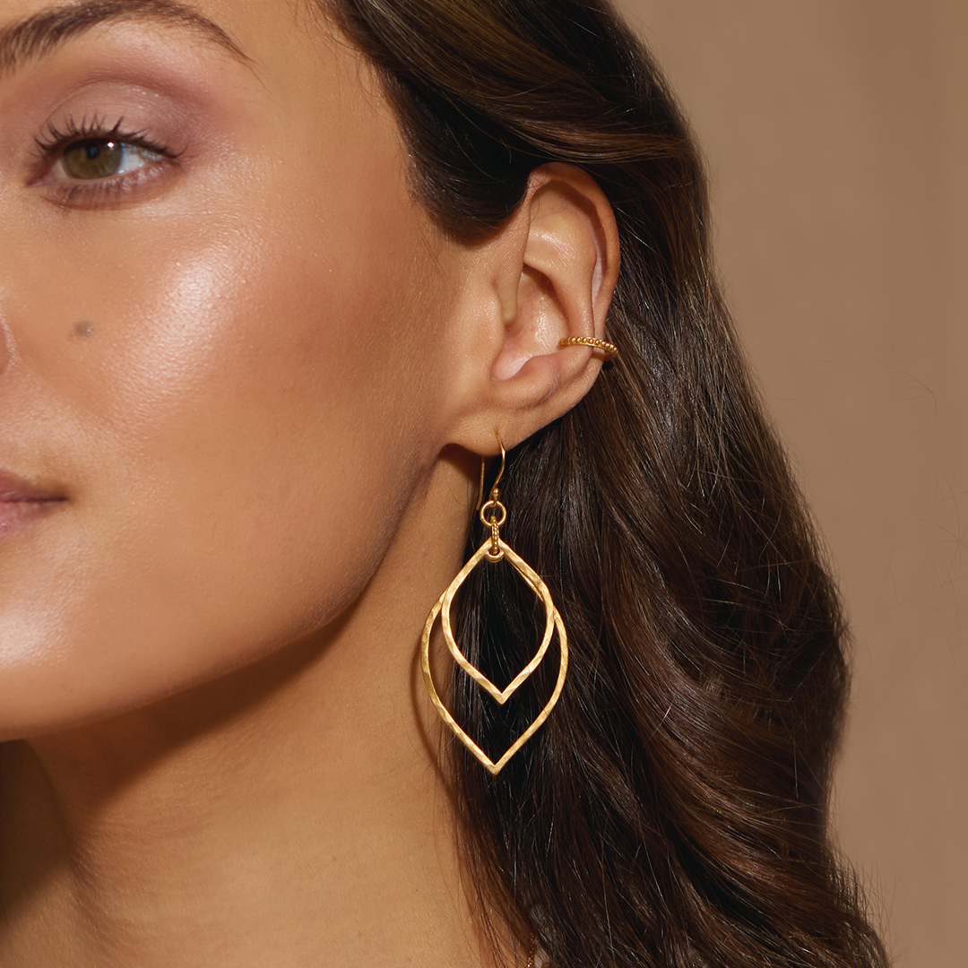 Close-up of a model wearing the Transformed by Light Lotus Linear Earrings, highlighting their shimmering gold design. This spiritual jewelry piece serves as a beautiful talisman for protection and embodies qualities of the sun and moon, enhancing yoga and meditation rituals.